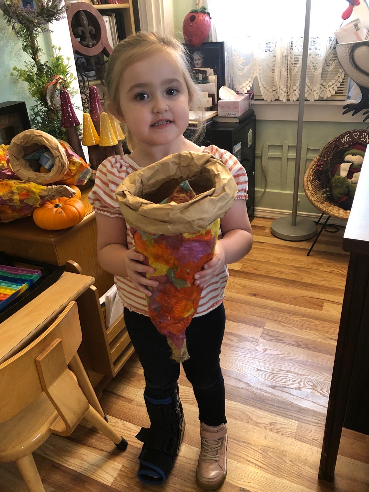 A girl proudly holds the paper-mache cornucopia she made