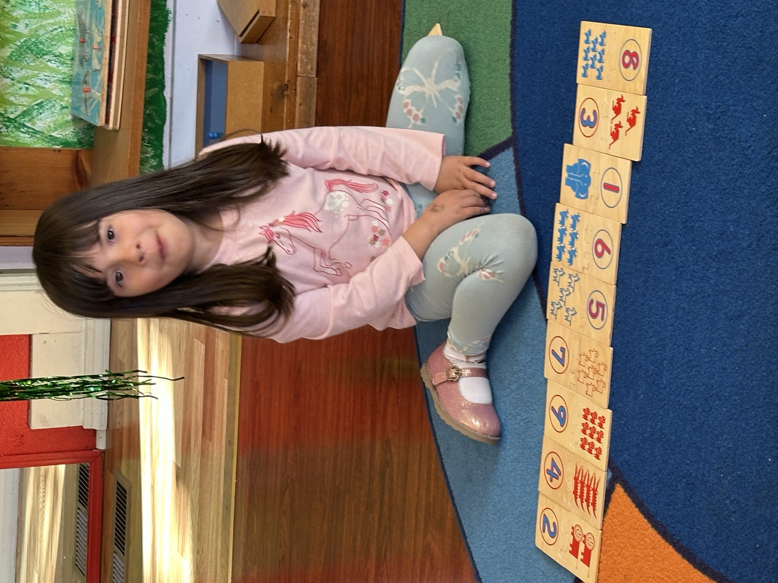 A girl arranges wooden counting tiles one to nine on the classroom rug