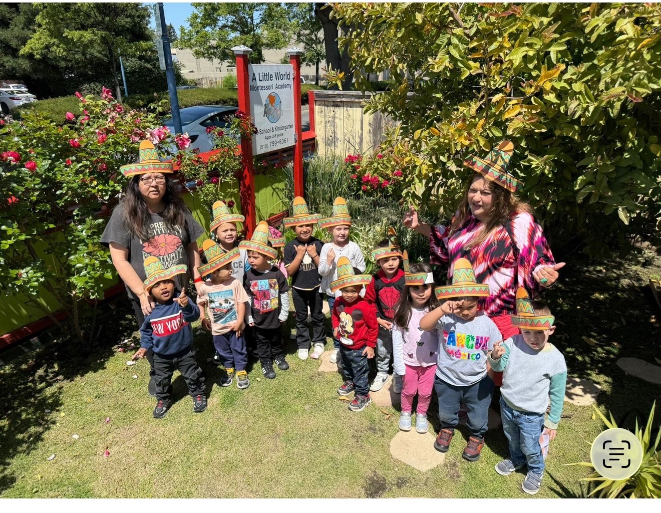Teachers and children in sombreros gather in the rose garden by the school sign