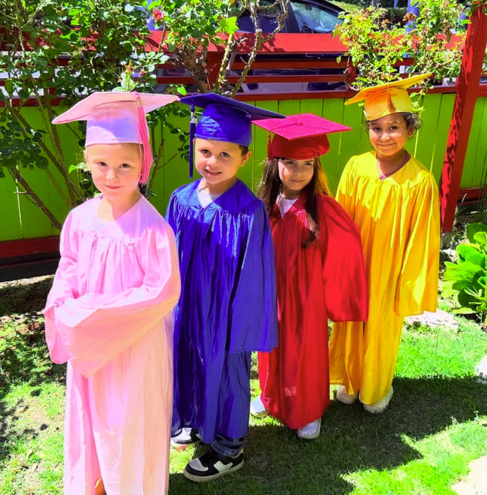 Four graduates in bright caps and gowns in the school garden