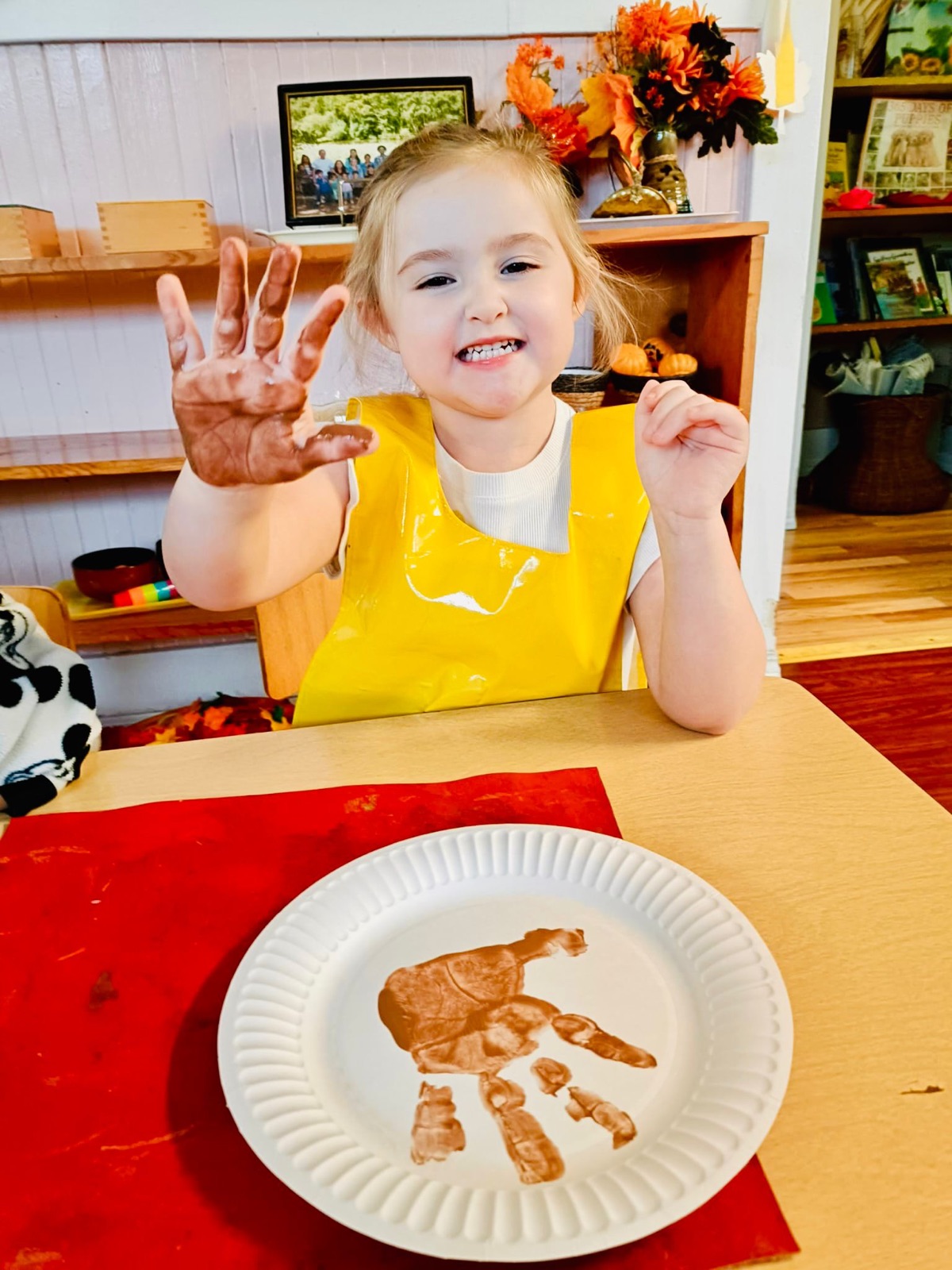 A smiling girl shows her paint-covered hand beside her handprint art