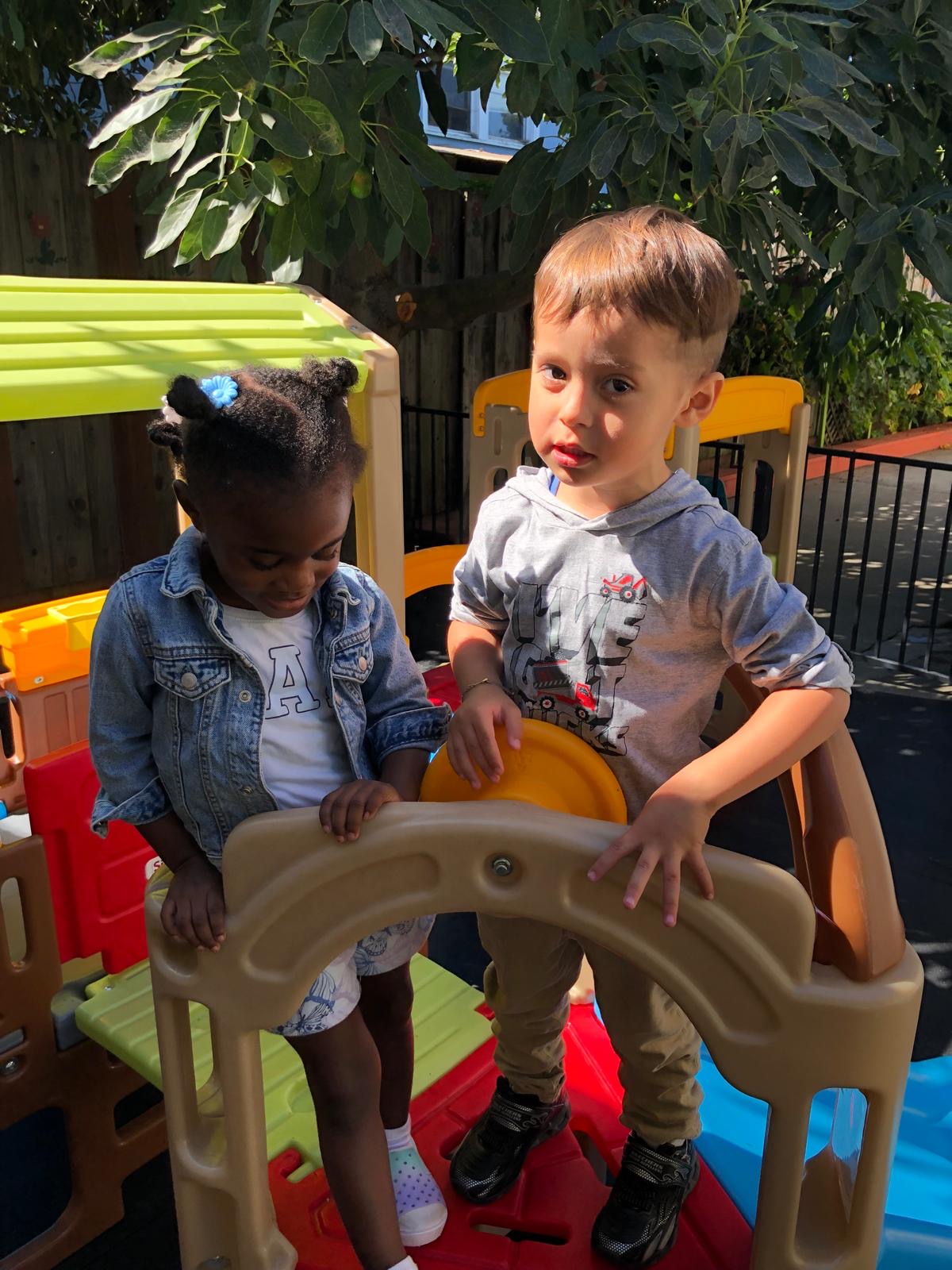 Two toddlers explore the playhouse structure in the play yard