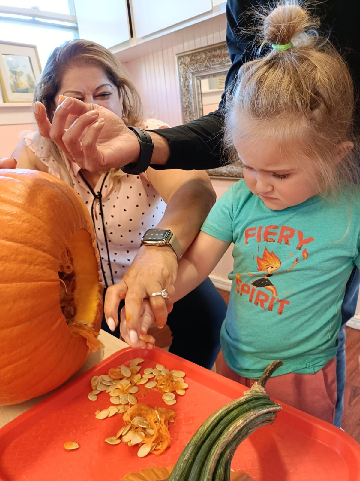A teacher and child scoop seeds from a big orange pumpkin